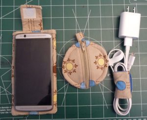 Matching phone case, circle earbud puoch and DIY cord keeper on a green background