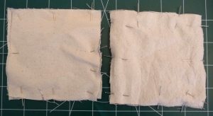 2 squares of cream fabric for hand warmers on a green background