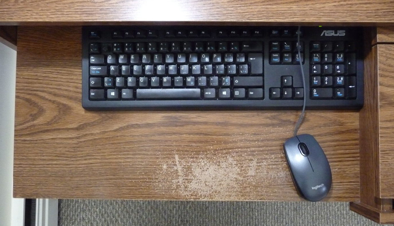 Black keyboard and mouse on a brown keyboard shelf with some damage