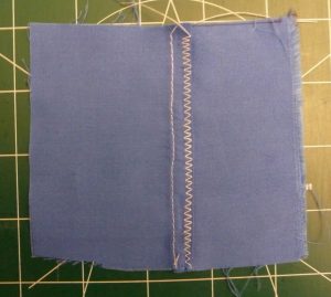 White thread used to sew a decorative flat felled seam in blue fabric