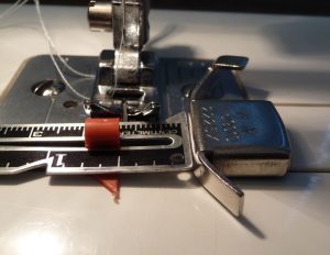 Close-up of sewing machine universal foot with seam gauge set to 1/2" and magnetic seam guide