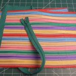 Dark green zipper laid obliquely across rectangle of colorful fabric with horizontal stripes