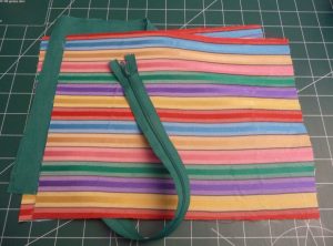 Dark green zipper laid obliquely across rectangle of colorful fabric with horizontal stripes 