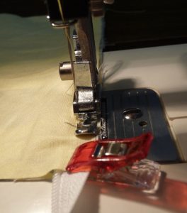 Close up of narrow zipper foot and red sewing clip being used to sew zipper onto yellow fabric