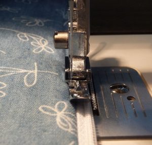 Close up of narrow zipper foot being used to top stitch along zipper
